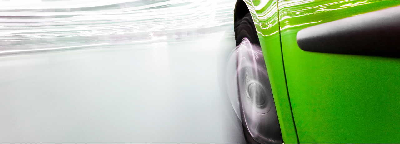 Close-up of front left wheel well area of green automobile with motion blur.