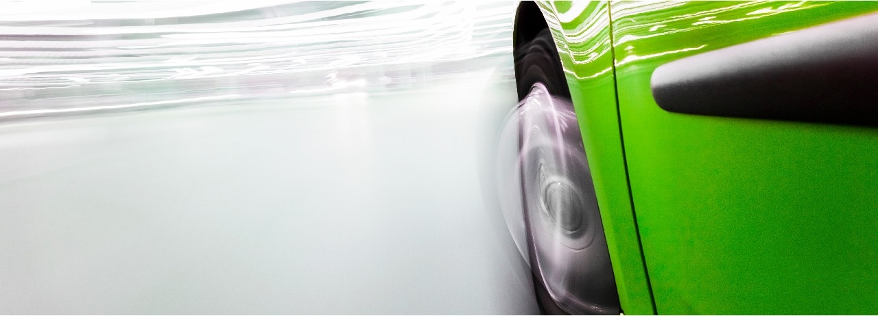 Close-up of front left wheel well area of green automobile with motion blur.